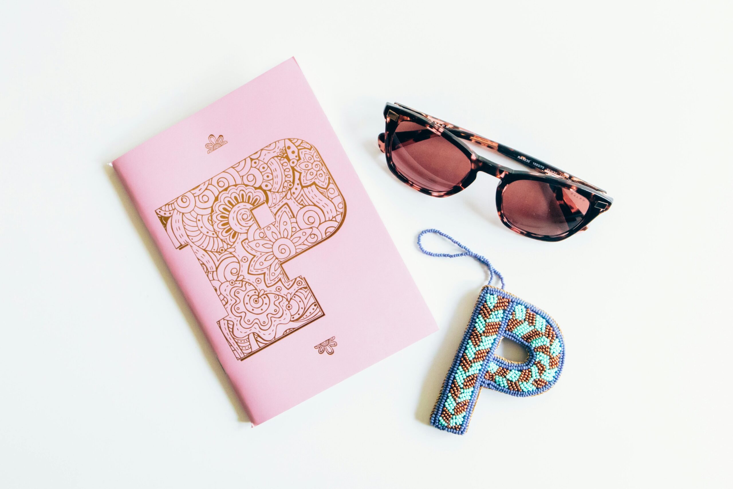 Aesthetic flat lay of a pink notebook and sunglasses on white background.