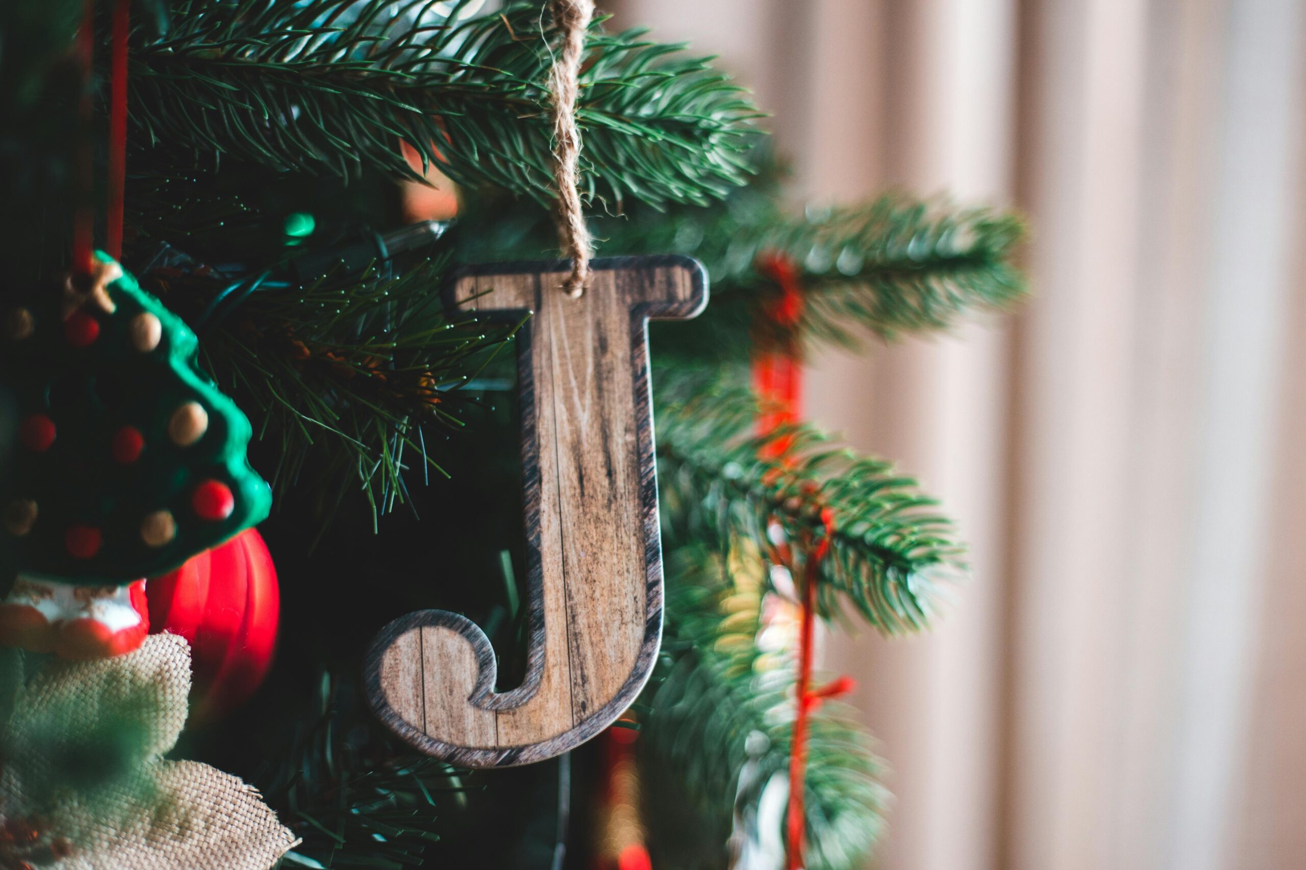 Wooden letter with rope hanging on coniferous tree sprig during New Year holiday in house